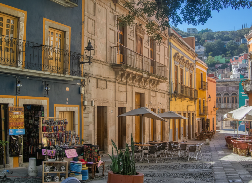 Cobblestone street scene in Guanajuato with colorful historic buildings and multiple outdoor restaurants/cafés. Where to eat in Callejón del Beso area.