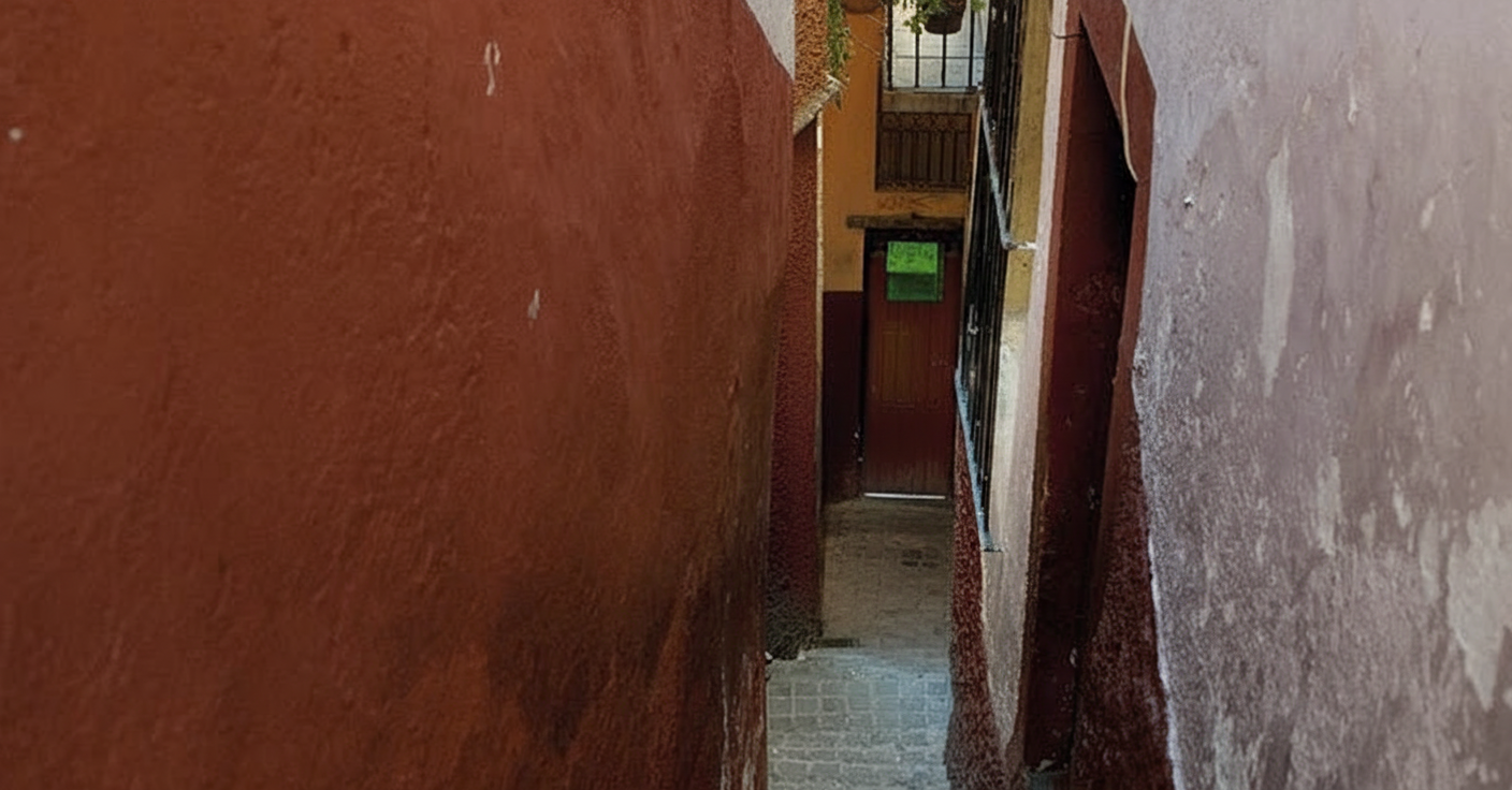 An extremely narrow, dark passage between two high, red-toned walls, characteristic of the side streets or sections of Callejón del Beso in Guanajuato, suggesting a confined space.